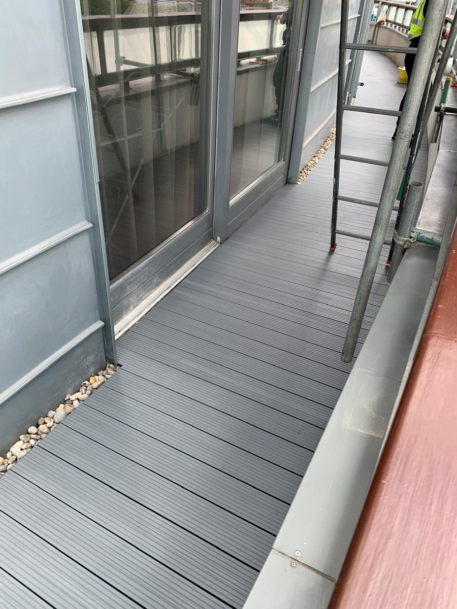 Newly installed grey Alideck aluminium decking along a balcony, with scaffold access alongside